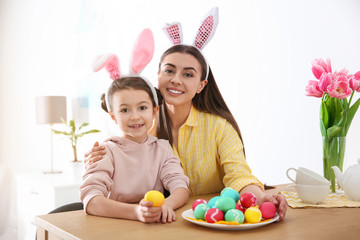 Mother and daughter with bunny ears headbands and painted Easter eggs at home