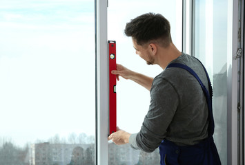 Construction worker using bubble level while installing window indoors