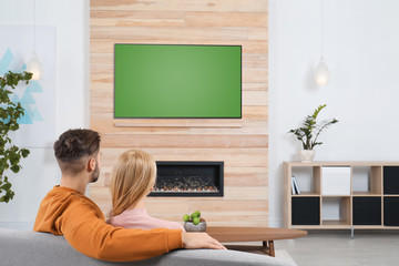 Couple watching TV on sofa in living room with decorative fireplace
