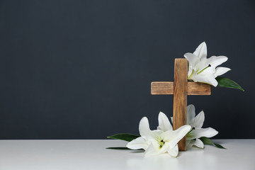 Composition with wooden cross and blossom lilies on table against color background, space for text