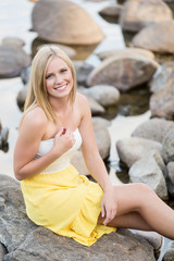 Attractive young woman sitting on river rocks