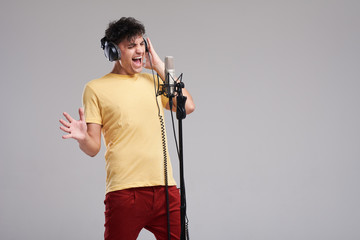 Portrait of rock singer man in studio professional headphones keeping static mic, sings a song...