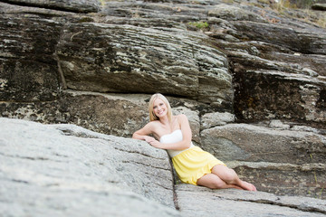 Beautiful young woman lying on river boulder