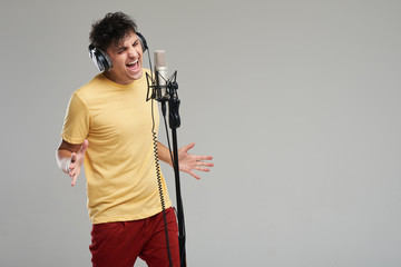 Portrait of rock singer man in studio professional headphones keeping static mic, sings a song...