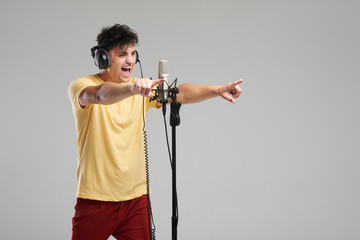 Portrait of rock singer man in studio professional headphones keeping static mic, sings a song...