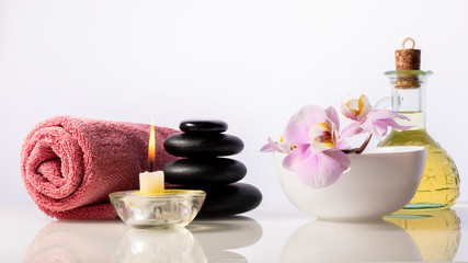 Fototapeta na wymiar Zen spa stones, orchid flower in bowl, candle, bottle with oil and towel. Spa composition isolated on white background.
