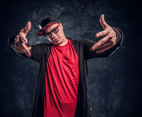 Portrait of a young rapper dressed in a hip-hop style, posing for a camera. Studio photo against a dark textured wall