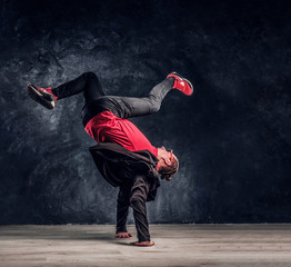 Hip-hop style dancer performs breakdance acrobatic elements. Studio photo against a dark textured...