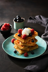 Freshly baked waffles with raspberries, berries, honey and coffee for breakfast or brunch on a dark background with copy space. Homemade Dessert concept.