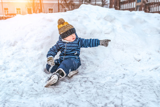 A small boy of 3-5 years old, in the winter outside in a snowdrift and snow, resting on a weekend, sitting in a blue jumpsuit and a warm hat. Snow on the background.