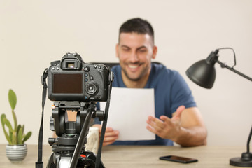 Young smiling cheerful man sitting at the office desk in front of the camera making a video. Male blogger recording a video tutorial.