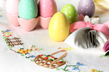 Easter place setting on an elegant embroidered linen table cloth with pink tulips and Easter eggs.   