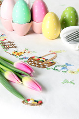 Easter place setting on an elegant embroidered linen table cloth with pink tulips and Easter eggs.   