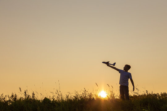 Black silhouette of happy caucasian child boy playing with toy airplane outside in meadow on sunny sunset time. Dreaming, imagination, curiosity concept. Horizontal color photography.