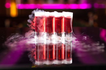 Four red cocktail shots with smoke on reflective mirror table