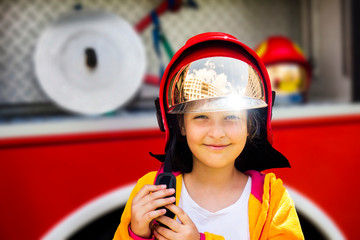 Fototapeta na wymiar Cute young girl trying on real fireman's helmet standing in front of firetruck.