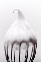 Metal whisk with whipped egg whites on white background