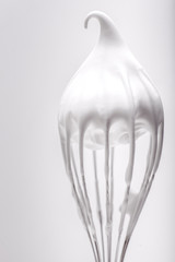 Metal whisk with whipped egg whites on white background