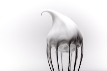 Metal whisk with whipped egg whites on white background
