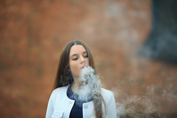 Vape teenager. Young pretty white girl in white cardigan smoking an electronic cigarette opposite...