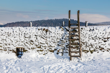 Snow covered dry stone wall in the Derbyshire Peak District,  Ladder style against a cold blue sky.