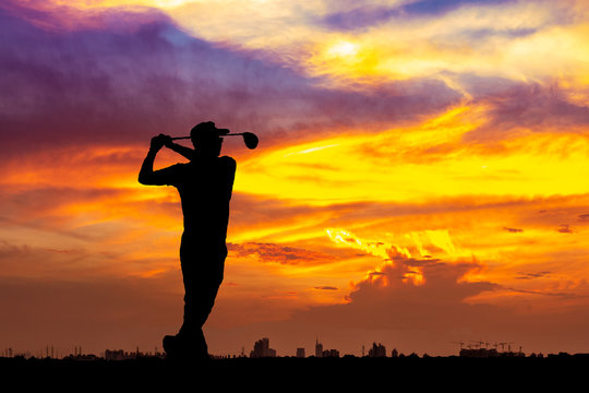 Silhouette of golfer hit sweeping on sunset background. Golfer young man playing golf during beautiful sunrise sky with city.