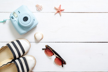 Fototapeta premium Summer holiday composition, traveler accessories on white wooden desk: sunglasses, sandals, instant camera, sea shell and star. Vacation, relaxing, sea beach resort, summer holidays concept