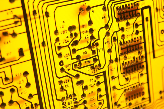 Yellow printed circuit board on the lighting. Soldering side of the PCB. Technological background with a circuit board texture. Selective focus.