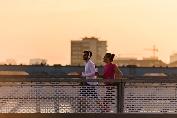 Young man and woman jogging together over bridge in the sunset