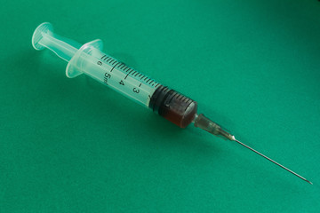 Medical syringe with needle and blood isolated on black and green background.