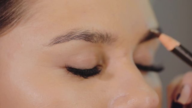 Tattoo artist makes a professional eyebrow correction, beautician contours eyebrows with a pencil