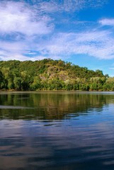 Reflection of green forest trees, blue sky and clouds in the calm flowing river