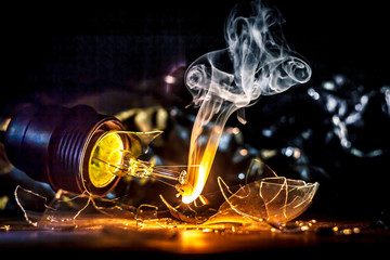 Amazing explosion of burning light bulb with splinters of broken glass and smoke on isolate black background. Сoncept of creative art illustrations of tungsten filament combustion in contact with air