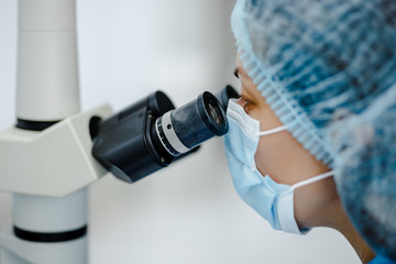 Researcher gaze into the eyepieces of a large laboratory microscope against a blurred background of...