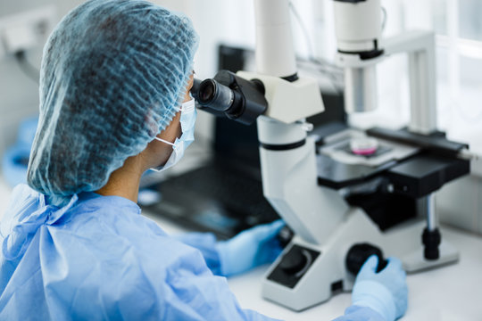 The doctor is looking through a microscope with a scientific and medical topic. A scientist and a laboratory technician are looking under a microscope to examine blood products of animals and chemical