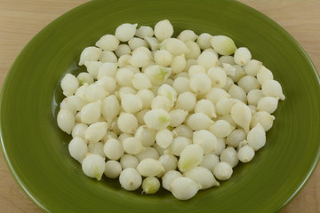 Close up of frozen pearl onions defrosting on green plate on wooden table