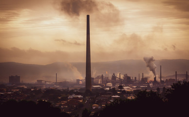 High view across industrial town to steel works and smoke stacks on stormy atmospheric evening. Old...