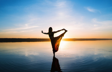 Silhouette woman on the beach at sunset doing yoga asana. Morning natural stretch warm-up training