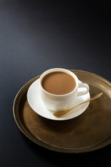 Milk coffee in white cup and saucer. Black moody background.