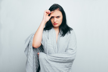 Upset girl in a gray robe indicates poor skin, age wrinkles, acne on a white and gray studio background. A woman is looking for flaws and age changes.