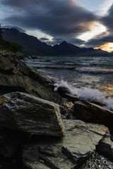 peaceful landscape during sunset with dramatic sky above the lake and mountain range, rocks in the foreground