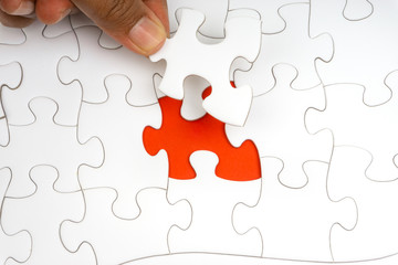 Fototapeta premium Hand put the last piece of jigsaw puzzle closeup to complete the mission. Selective focus and crop fragment