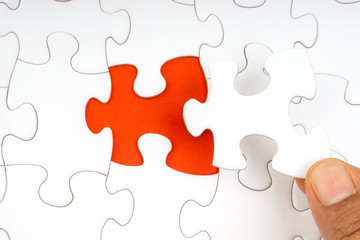 Fototapeta premium Hand put the last piece of jigsaw puzzle closeup to complete the mission. Selective focus and crop fragment