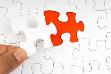 Fototapeta premium Hand put the last piece of jigsaw puzzle closeup to complete the mission. Selective focus and crop fragment