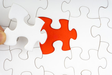 Fototapeta premium Hand put the last piece of jigsaw puzzle closeup to complete the mission. Selective focus and crop fragment