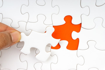 Fototapeta premium Hand put the last piece of jigsaw puzzle closeup to complete the mission. Selective focus and crop fragment
