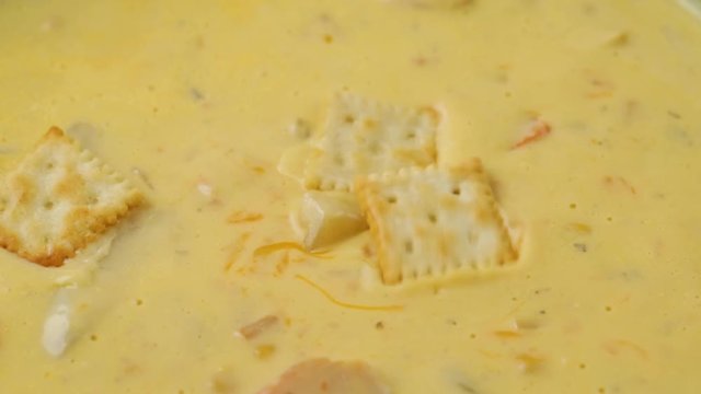 Close video of adding crackers to chicken corn chowder with cheese illuminated with natural lighting.