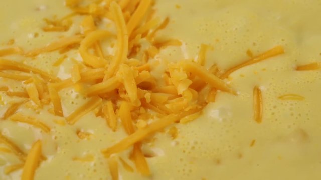 Very close video of adding extra shredded cheddar cheese to chicken corn chowder while cooking illuminated with natural lighting.