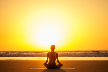 Silhouette of young woman in a stylish suit for yogi jumpsuit doing yoga on the beach in pose copy space