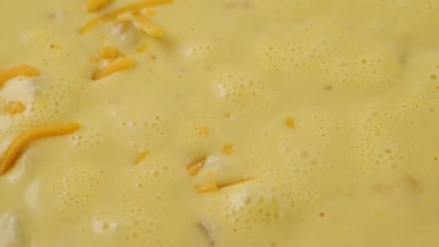 Very close video of adding shredded cheddar cheese to chicken corn chowder while cooking illuminated with natural lighting.
